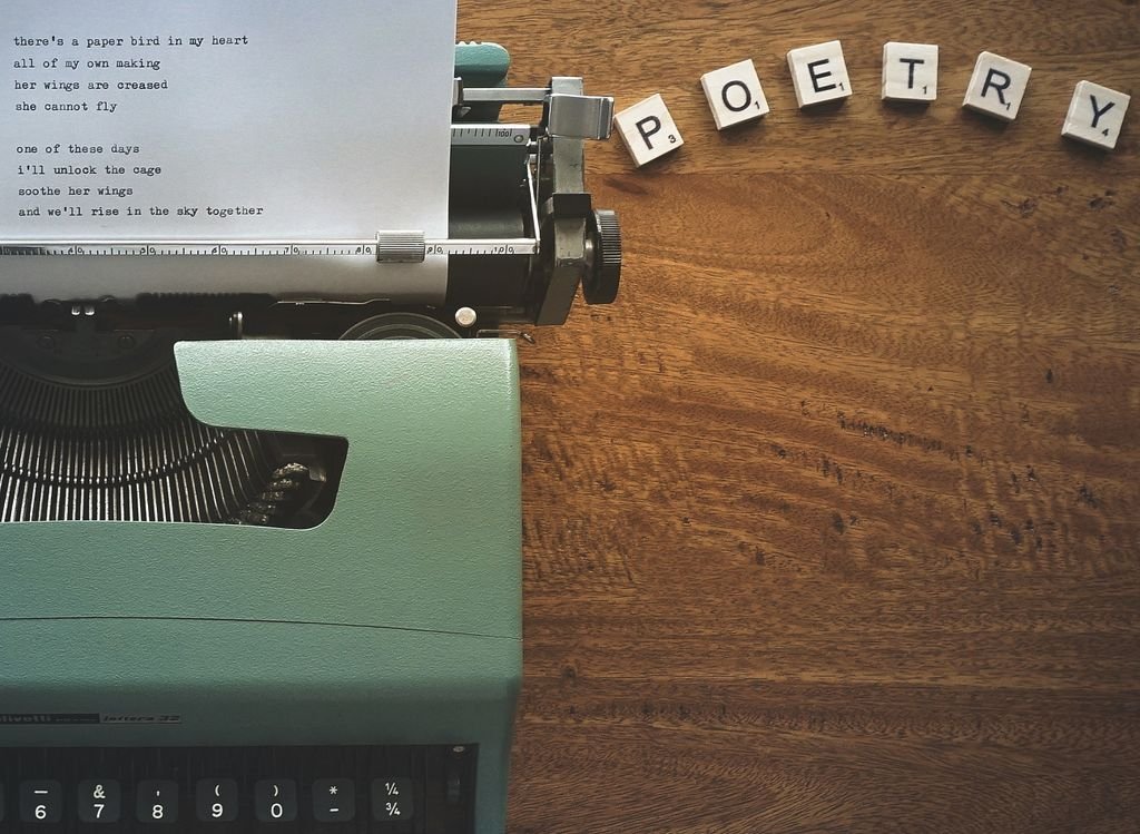 A typewriter creates poetic lines on paper amidst Scrabble tiles spelling 'POETRY'.