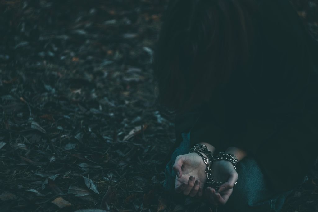 A person sits outdoors on fallen leaves, hands chained, evoking themes of restraint and solitude.